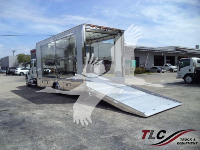 Truck bed with wheelchair-accessible ramp and glass-sided cargo area, International MV rollback truck in a lot.