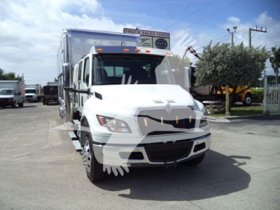 Truck front view of a white 2027 International MV rollback tow truck with a silver cab and a large aluminum box body in a dealership lot.