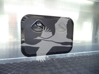 Trailer side window with two circular vents and a protective panel; metal surface and diamond plate floor visible.