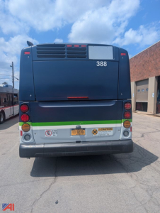 Rear view of a 2013 New Flyer XD60 transit bus showing license plate area, taillights, rear bumper, and safety decals.