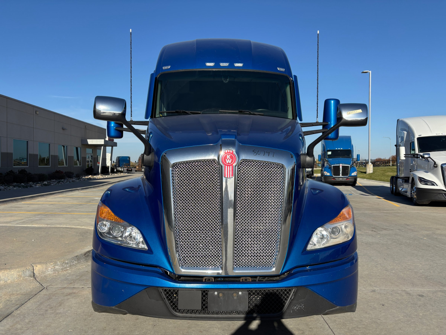 Kenworth T680 truck front grille and cab exterior in blue, showroom-like lot, with side mirrors and Kenworth emblem visible.