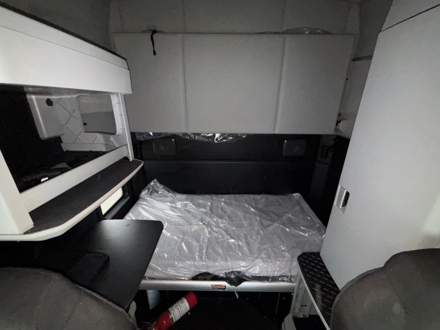 Kenworth T680 sleeper cab interior showing bed platform in cabin with storage cabinet on left and step on right, plastic covering on mattress.