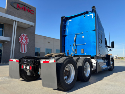 Blue Kenworth T680 sleeper tractor from rear three-quarter view showing dual rear axles and chassis with mud flaps.