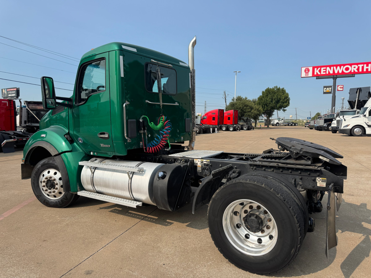 Kenworth T880 cab and chassis showing fuel tanks and wheel at front, side view with green cab and black chassis, dealership lot in background.