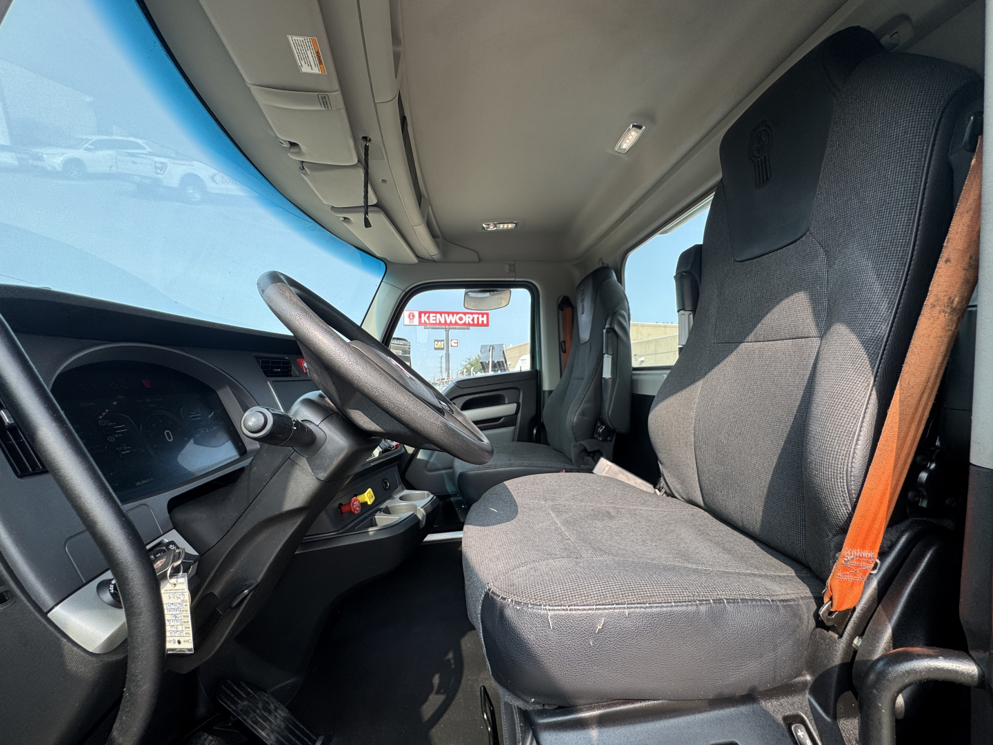 Kenworth T880 cab interior showing steering wheel and driver's seat with gray fabric, dashboard and window view