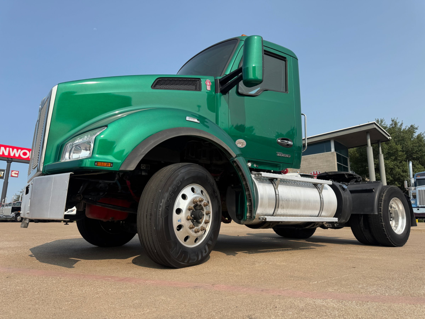 Kenworth T880 conventional daycab truck side view showing green cab and front wheel, fuel tank, chassis, and wheel well.