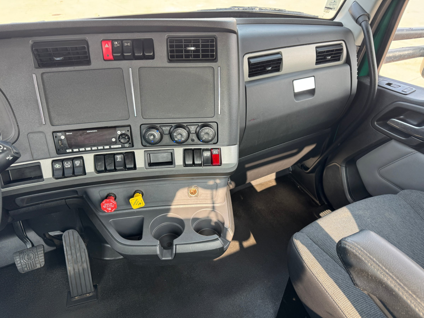 Truck cab dashboard of a 2022 Kenworth T880 showing steering column area, ignition, climate controls, ... various switches and cup holders visible.