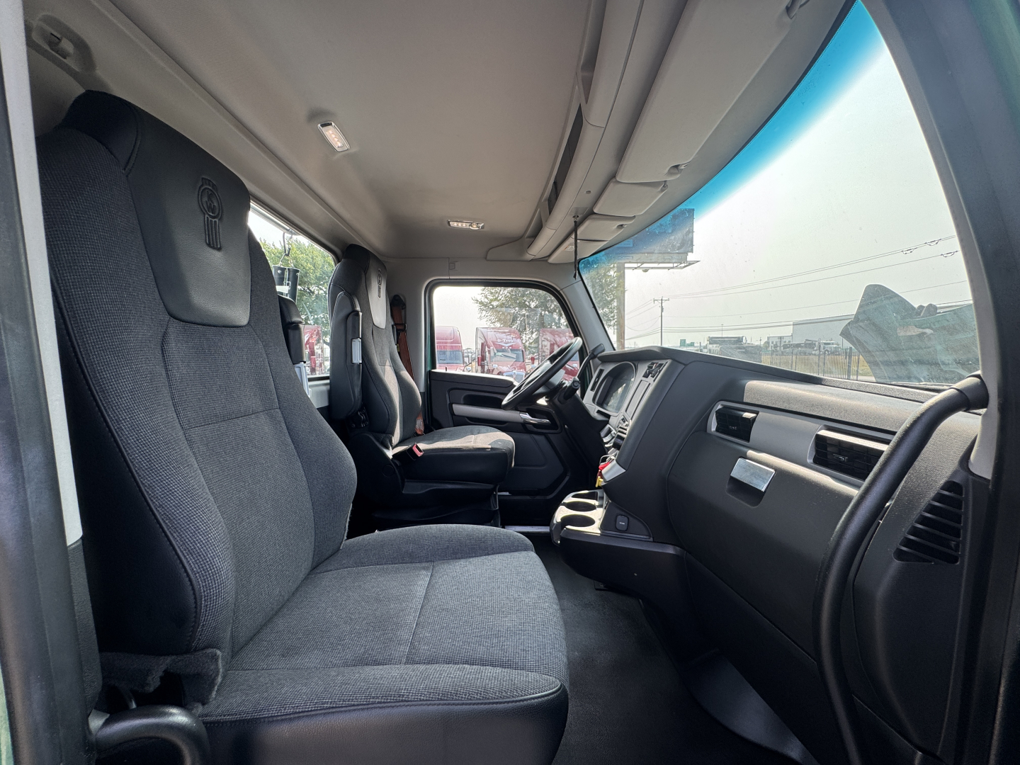 Interior of a 2022 Kenworth T880 cab showing front seats, dashboard, and steering wheel from the passenger side with gray upholstery.