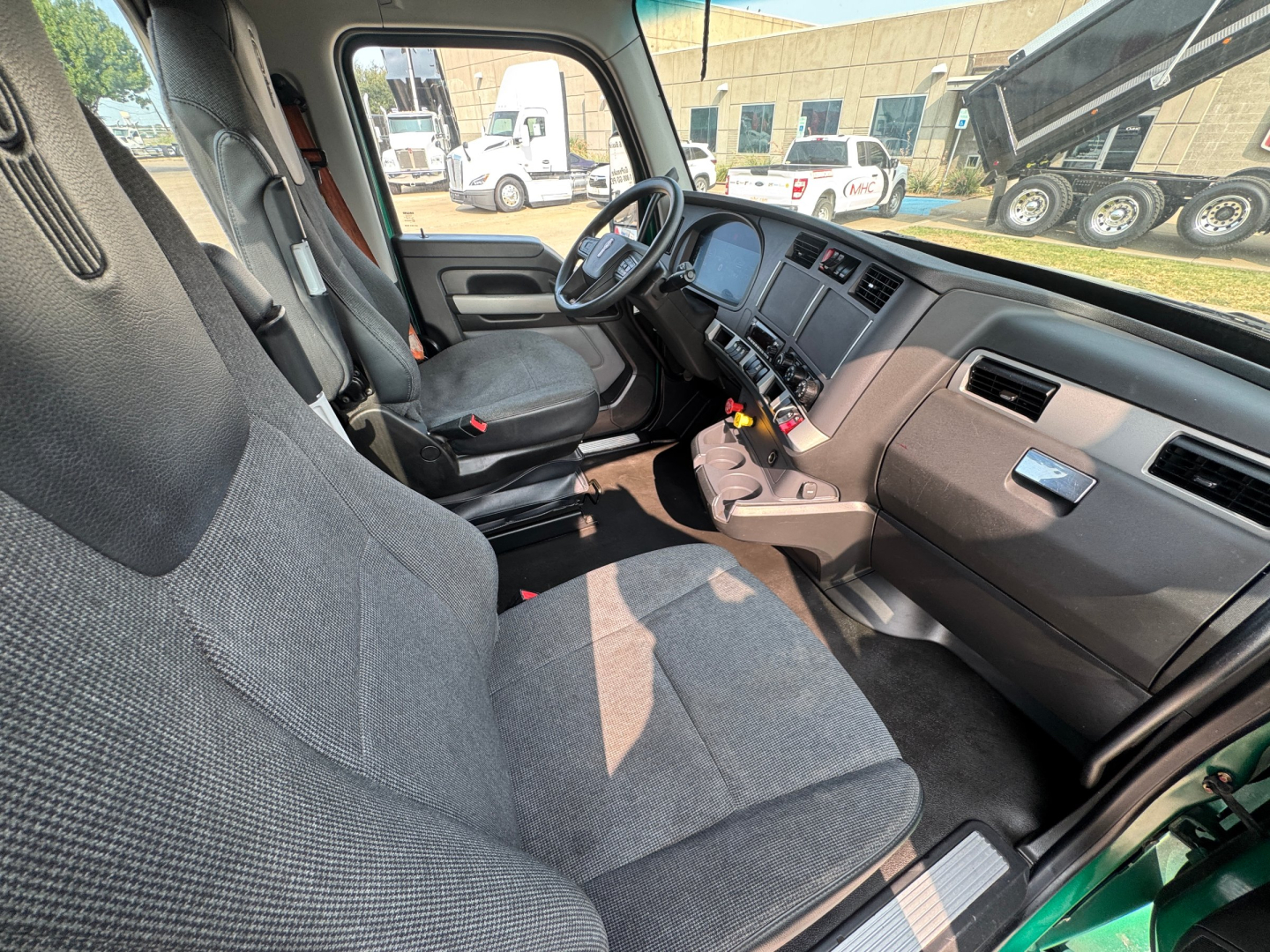 Interior front cabin of a 2022 Kenworth T880 conventional daycab showing two gray cloth seats, steering wheel, dashboard, and center console viewed from the passenger side.