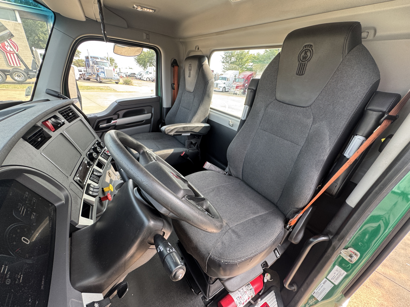 Kenworth T880 truck interior showing driver seat and steering wheel with dashboard and passenger seat. Visible are command controls, steering column, and gear lever.