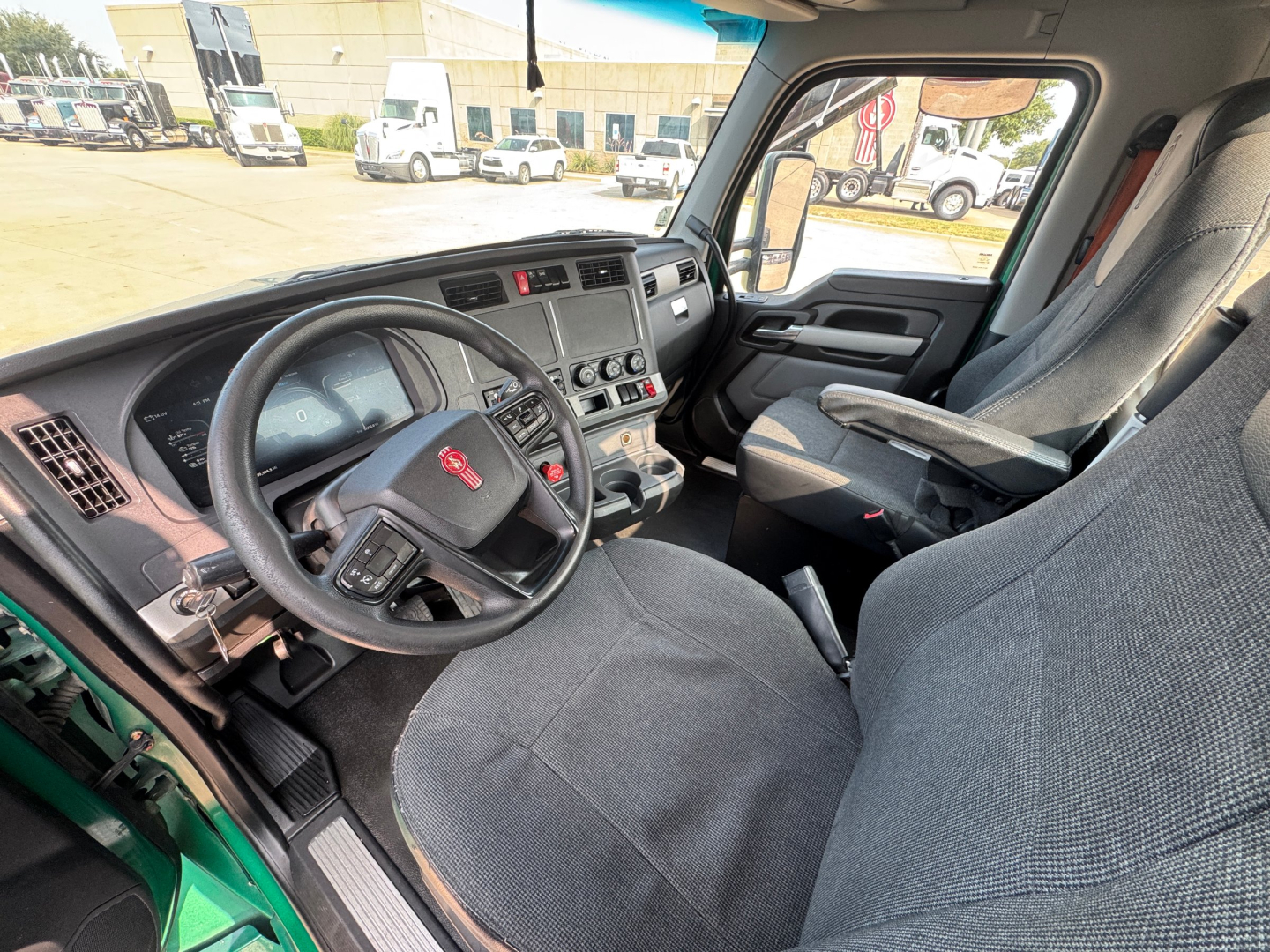 Kenworth T880 cab interior showing steering wheel, dashboard, and driver seat with controls and center console; view through open door.