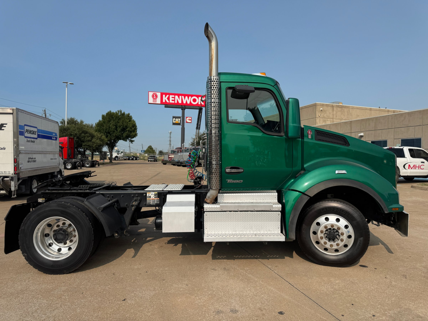 Kenworth T880 side view showing green cab and chassis with vertical exhaust, fuel tanks, and steps.