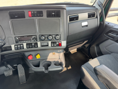 Truck cab dashboard of a 2022 Kenworth T880 showing steering column area, ignition, climate controls, ... various switches and cup holders visible.
