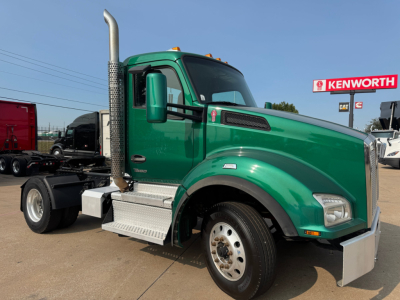 Green Kenworth T880 daycab truck in a dealership lot, side view showing cab, chrome exhaust stack, silver steps, and front bumper.
