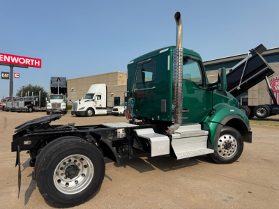 Kenworth T880 daycab tractor in green with exposed exhaust stack and chassis, side view showing rear frame and wheel, dealership lot in background.