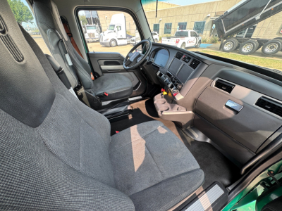 Interior front cabin of a 2022 Kenworth T880 conventional daycab showing two gray cloth seats, steering wheel, dashboard, and center console viewed from the passenger side.