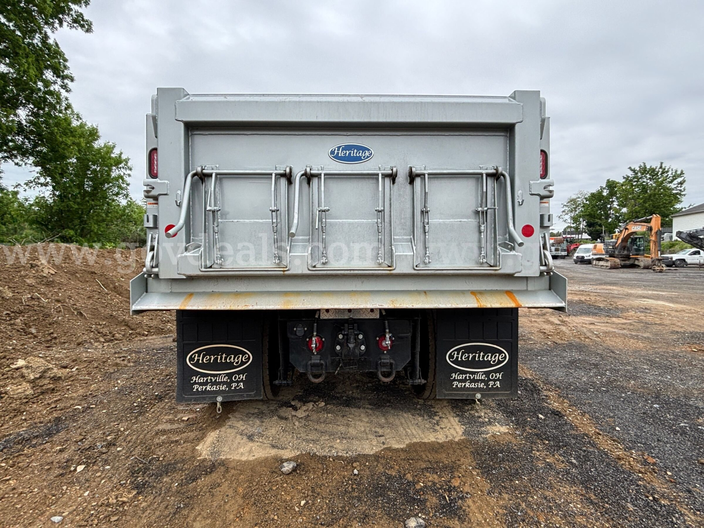 Dump truck rear showing Heritage brand tailgate and dual mudflaps with Heritage decals, steel bed, hydraulic hookups, and rear lights.