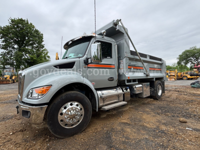 Kenworth T380 dump truck in service showing gray body with orange reflective stripes, chrome fuel tanks, dual rear wheels, dump bed, front headlights and grille.