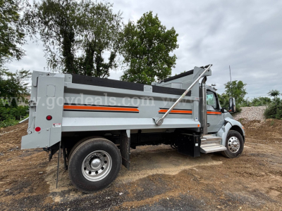 Kenworth T380 dump truck side view showing dump bed, hydraulic system, and wheel with tread, gray body with orange stripes.