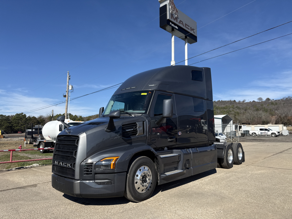 Truck in showroom lot showing 2026 Mack PR64T76H tractor with glossy dark gray paint and dual rear axles.