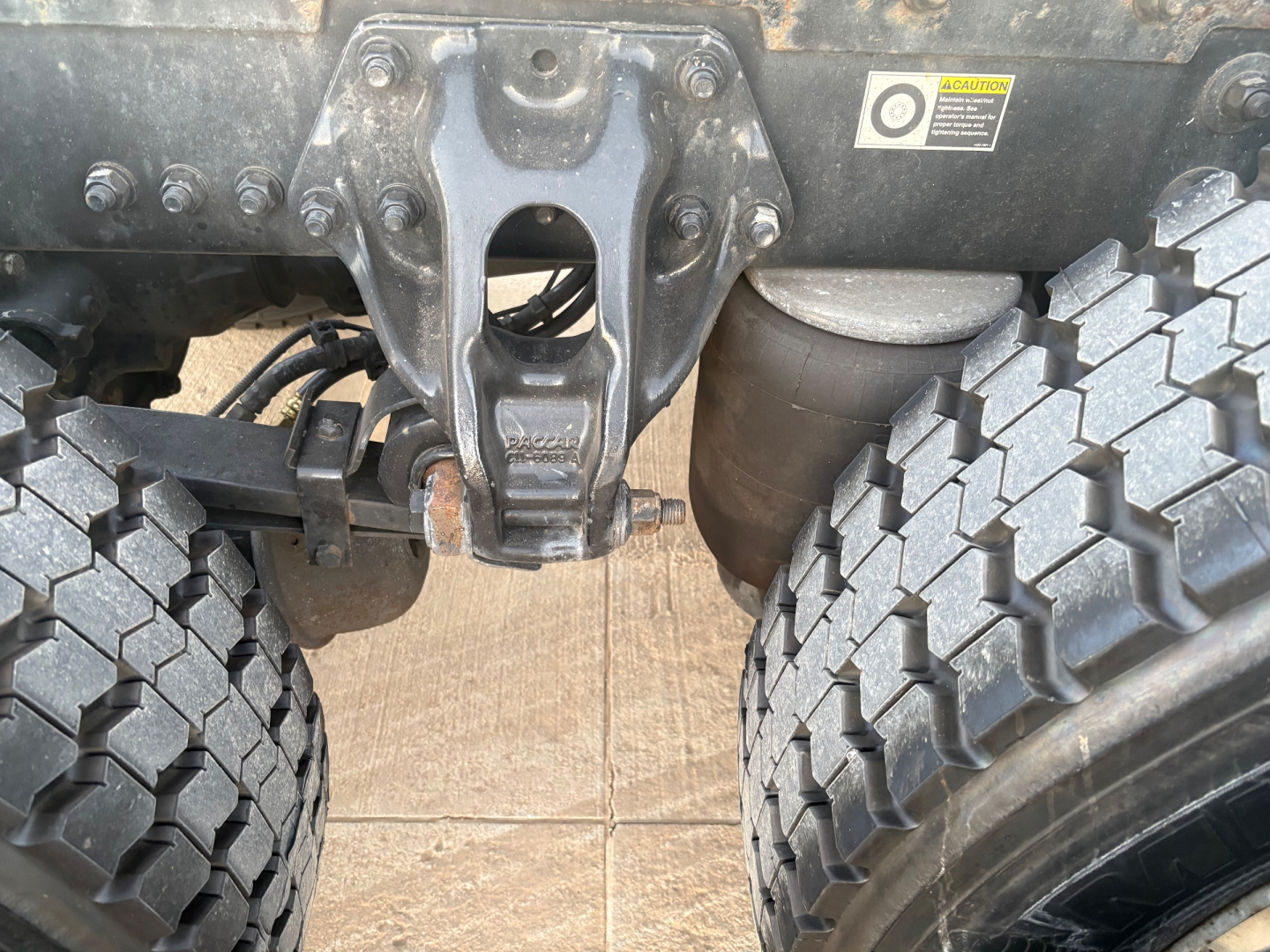 Kenworth T680 chassis view showing tag, rear suspension hanger, and dual rear tires with heavy tread.