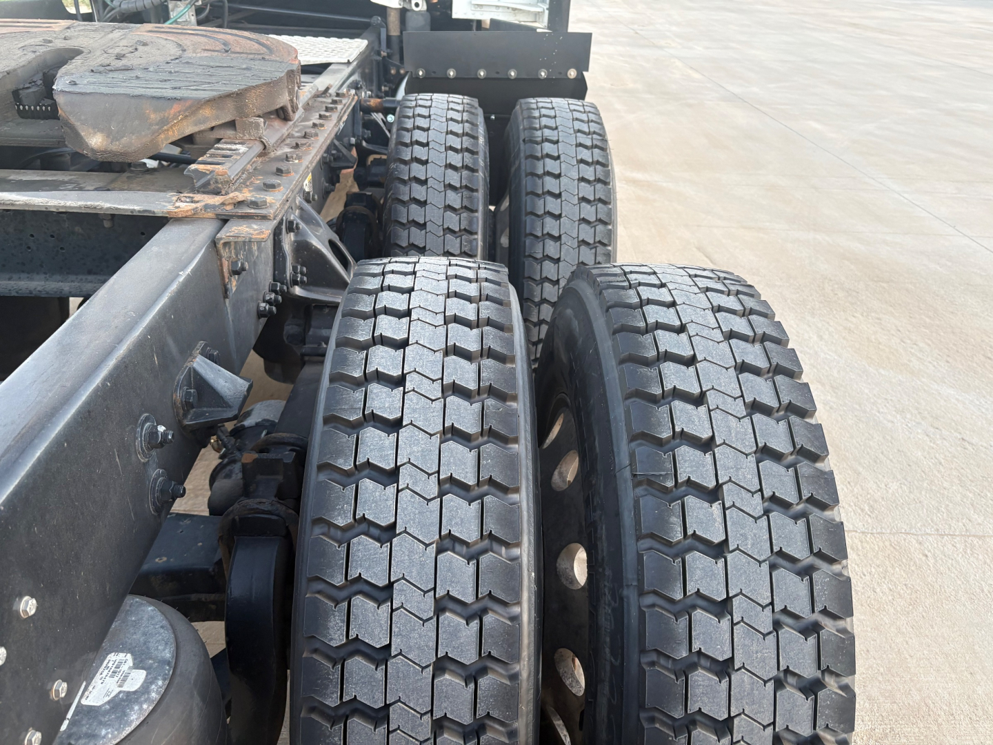 Kenworth truck chassis rear view showing dual rear axles with treaded tires and part of frame rails.