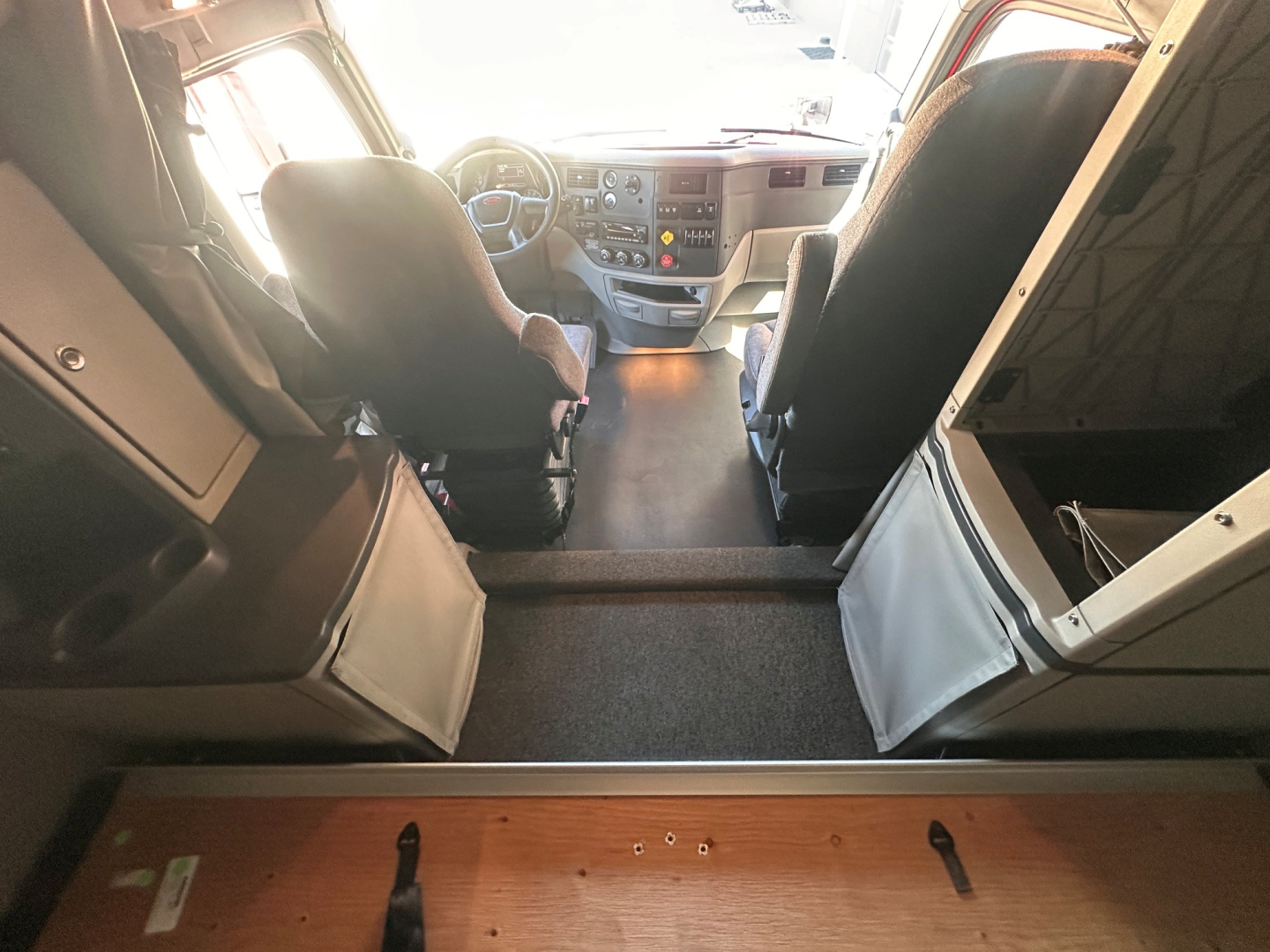 Peterbilt 579 cab interior from rear looking toward driver and passenger seats; dashboard and steering wheel visible; steps and floor between cab and sleeper area.