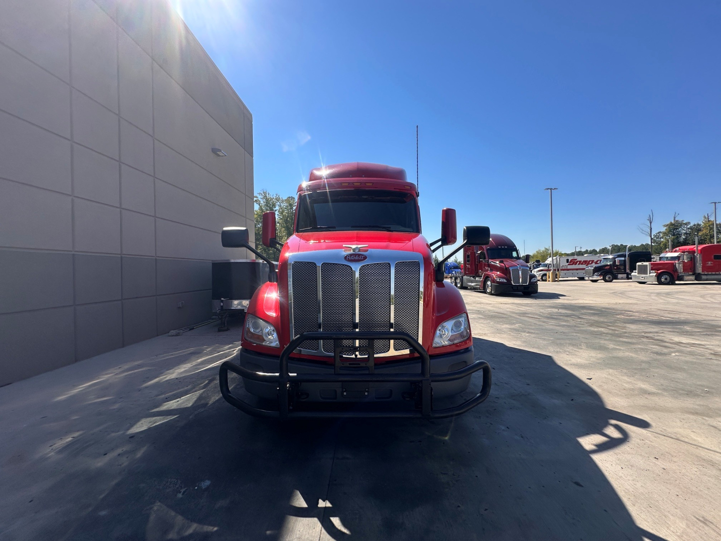 Peterbilt 579 truck front view with grille guard and chrome bumper, daytime outdoor lot, blue sky, other trucks in background.