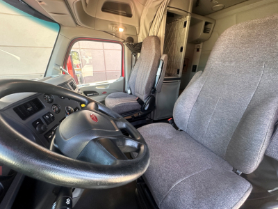 Peterbilt 579 truck cabin interior showing steering wheel, driver seat, and sleeper area with grey fabric upholstery.