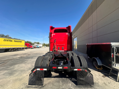 Peterbilt 579 tractor cab rear view showing fifth wheel and dual rear axles with mud flaps and red sleeper cab.