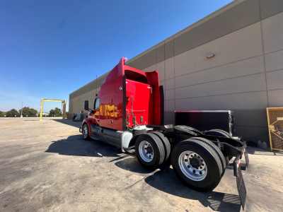 Peterbilt 579 sleeper cab tractor in red, side view showing rear dual axles and flatbed fifth wheel.