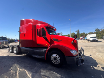 Peterbilt 579 truck in red with sleeper cab, side view showing front grille, headlights, and wheel; clear sky.