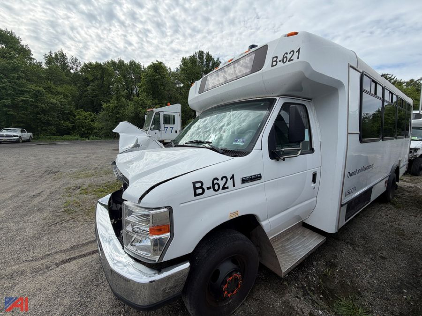 Bus front-left view of a white 2019 Ford E450 shuttle bus with heavy front-end damage and B-621 markings.