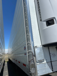 Trailer side with vertical rear corner showing 2018 Utility 3000R W, reefer trailer, aluminum side, reflective stripes, and access panel near front. Visible text includes VIN/ID near door and serial sticker on trailer front corner.