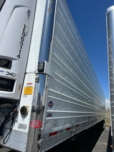 Utility 3000R W trailer side with metal ribbed walls, rear access latch, and small stickers showing specifications.