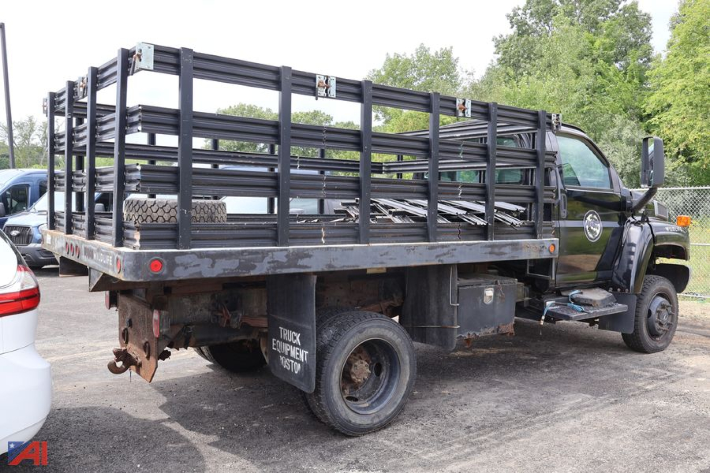 Flatbed dump truck with black metal side rails and stacked framework in bed, Chevrolet-style cab front, used tag on wheel well.