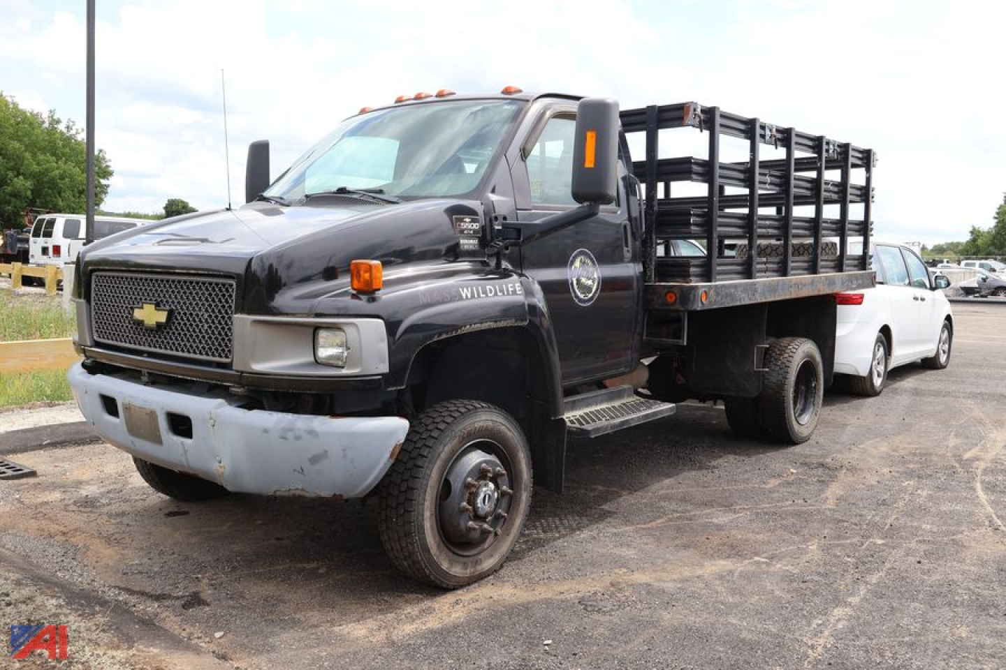 Chevrolet medium-duty dump truck with flatbed and side rails, black cab, white bumper, dual rear wheels, on a lot.