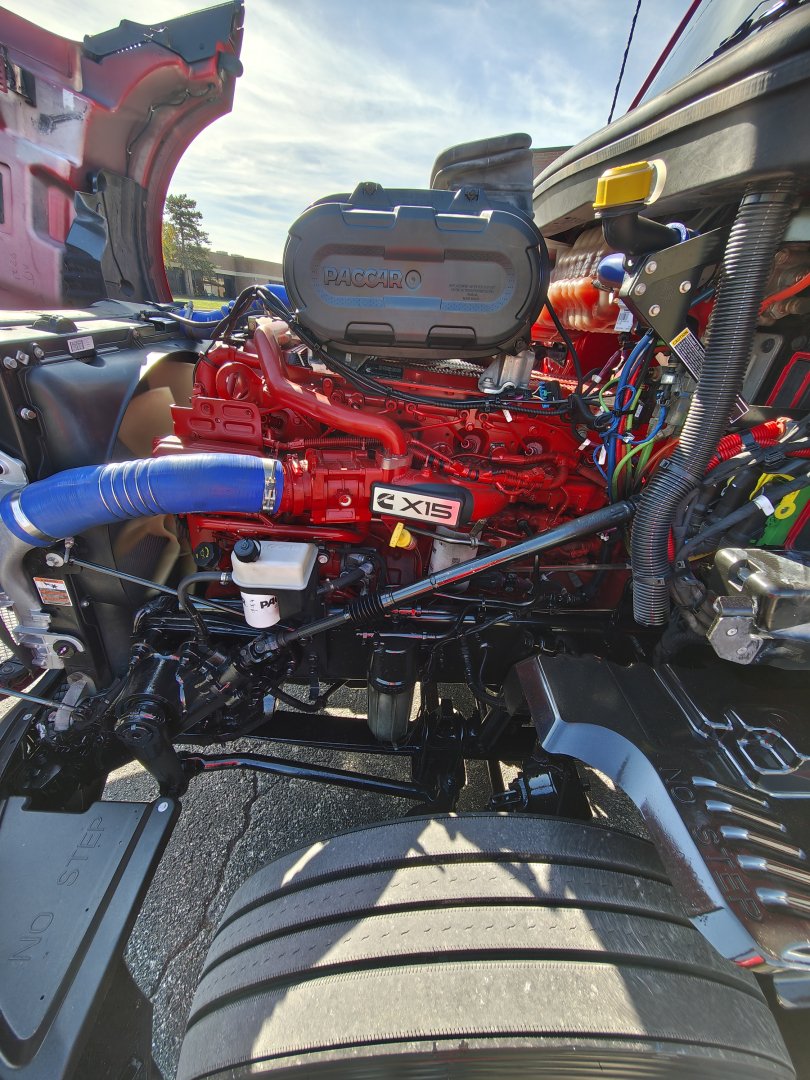 Kenworth T680 engine bay with bright red engine labeled 6x15 and blue silicone hose; visible battery box and wiring, hood open