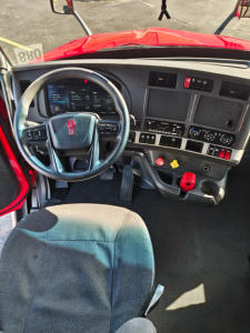 Kenworth T680 cab interior showing steering wheel, dashboard with digital display, control switches, and gear lever.