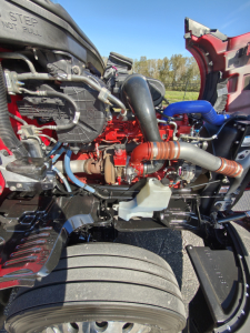Kenworth T680 engine bay with visible turbocharger, hoses, and intercooler piping in red and blue accents; radiator and air intake components in view.