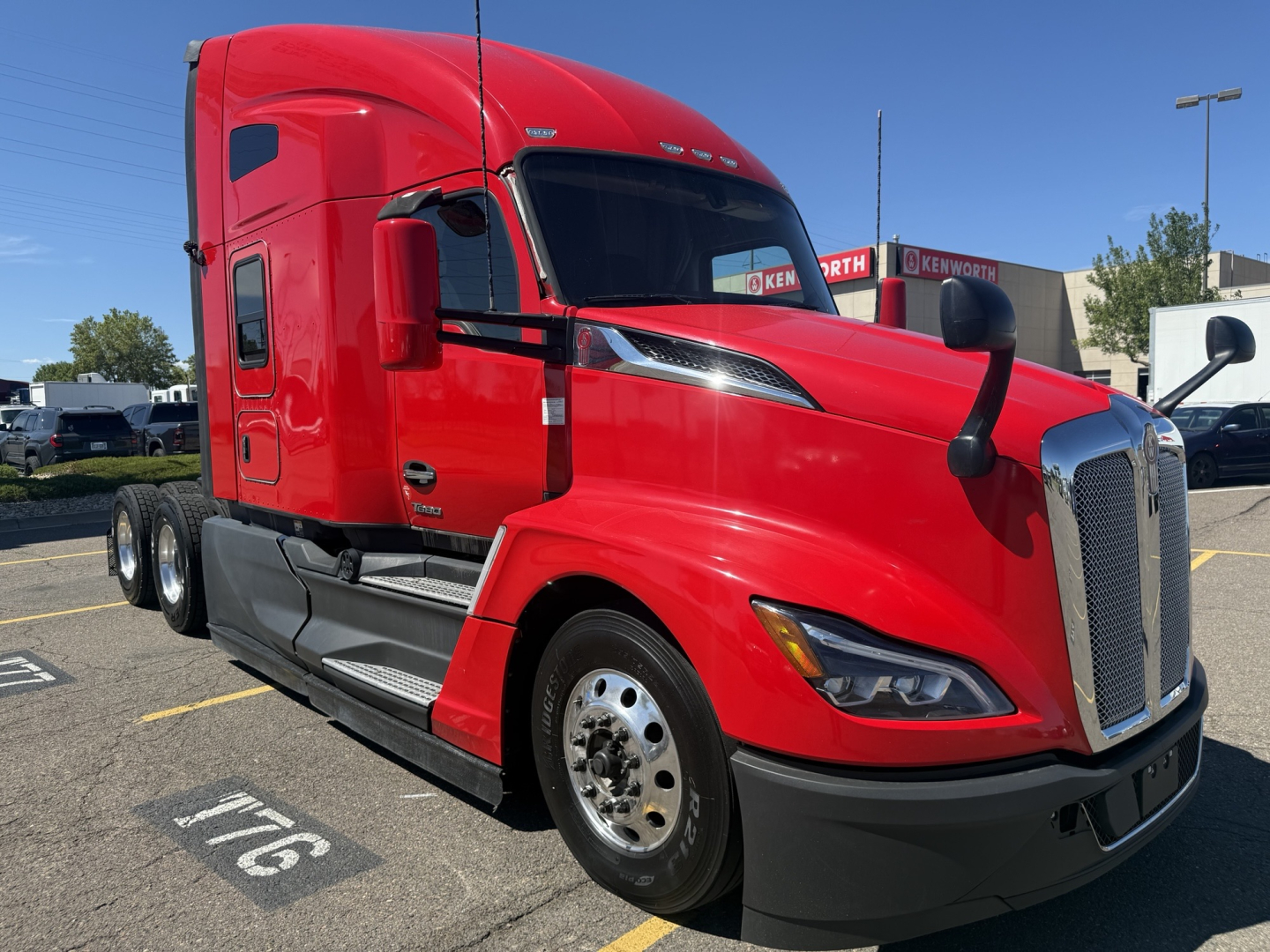Kenworth T680 conventional sleeper truck in red, front-side view showing two-axle tractor with chrome grille, large fuel tanks, and black bumper.
