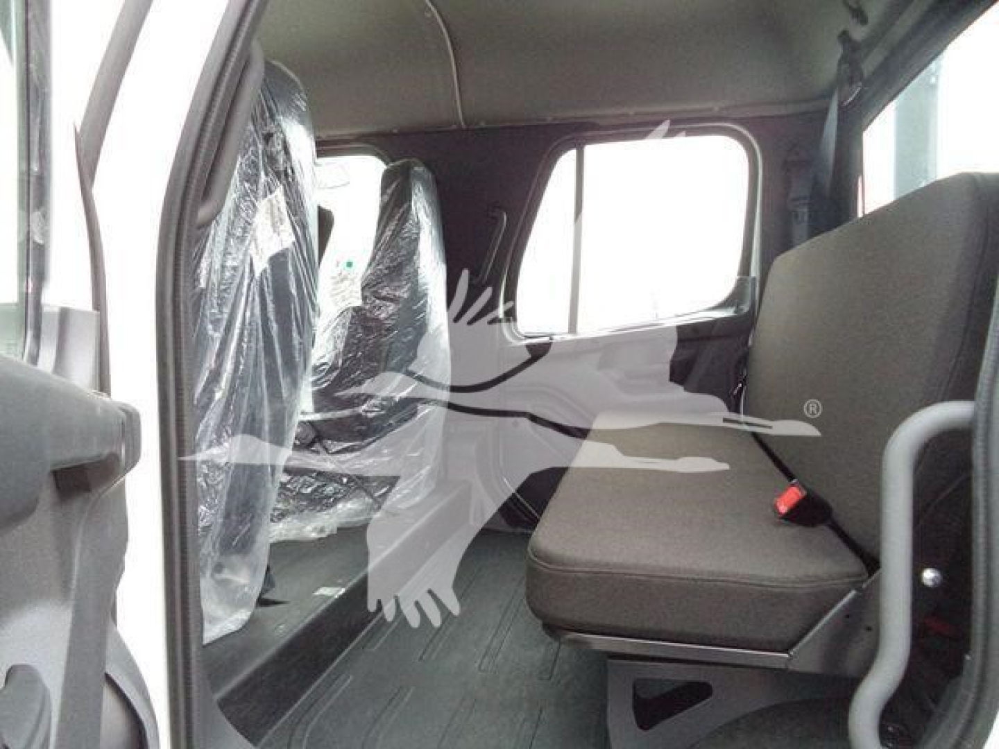 Cab interior of a Freightliner M2 106 rollback truck showing front passenger seat and rear seating area with plastic-covered seats and window light.