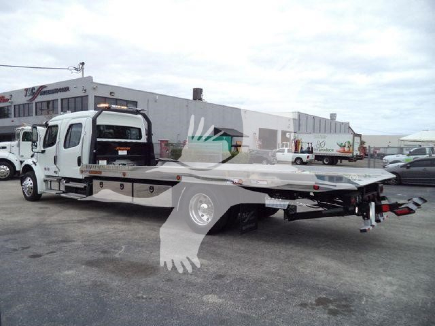 Flatbed tow truck on a lot with Freightliner M2 106 chassis and rollback bed, rear view showing winch and ramps.