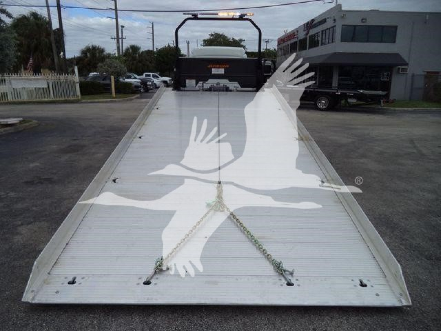 Flatbed truck bed with a ramp on Freightliner M2 106. Chain tie-downs visible on aluminum surface.