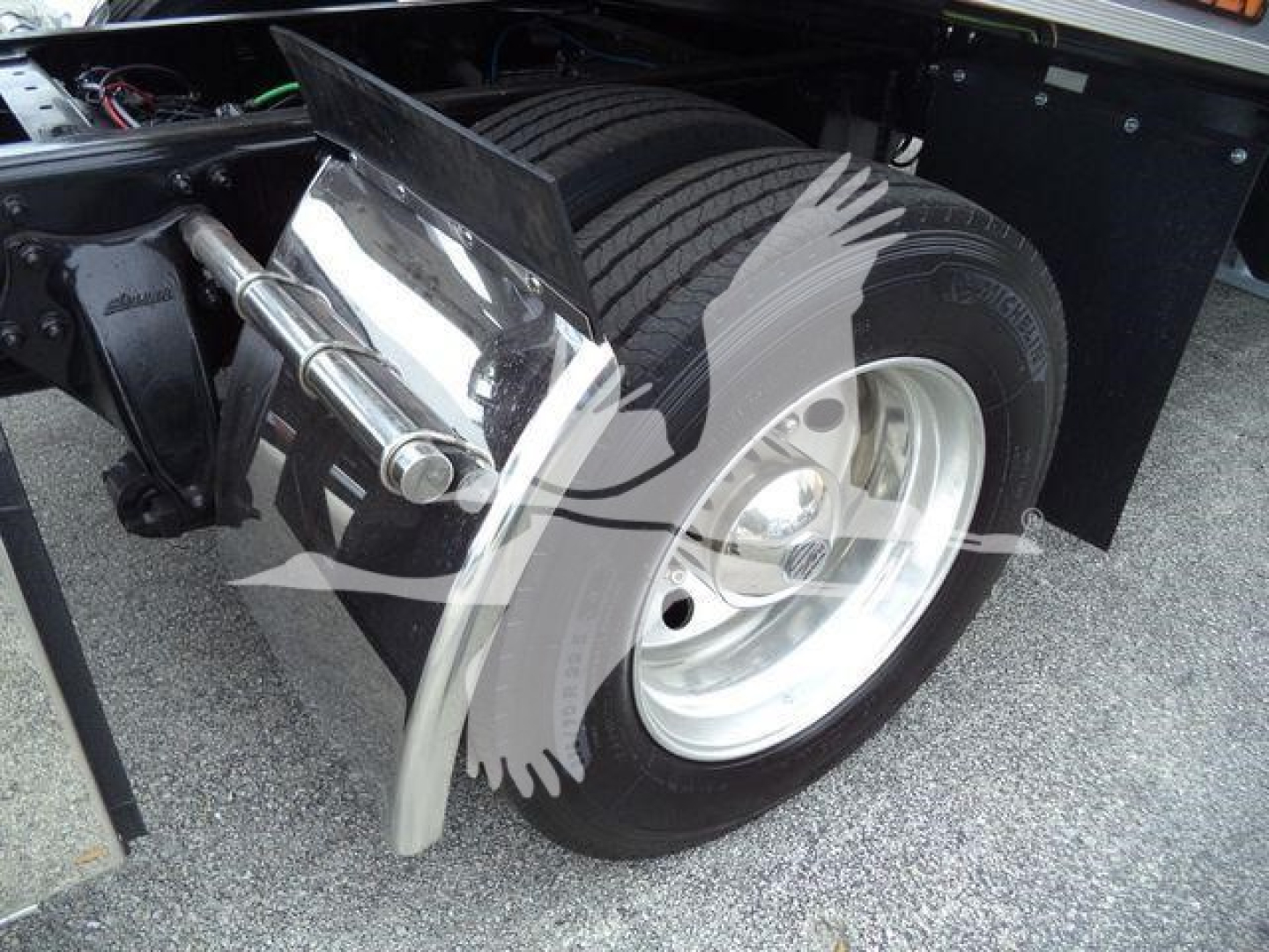 Truck rear wheel area showing suspension, dual rear tires, and fender splash guard on Freightliner M2 106 chassis.