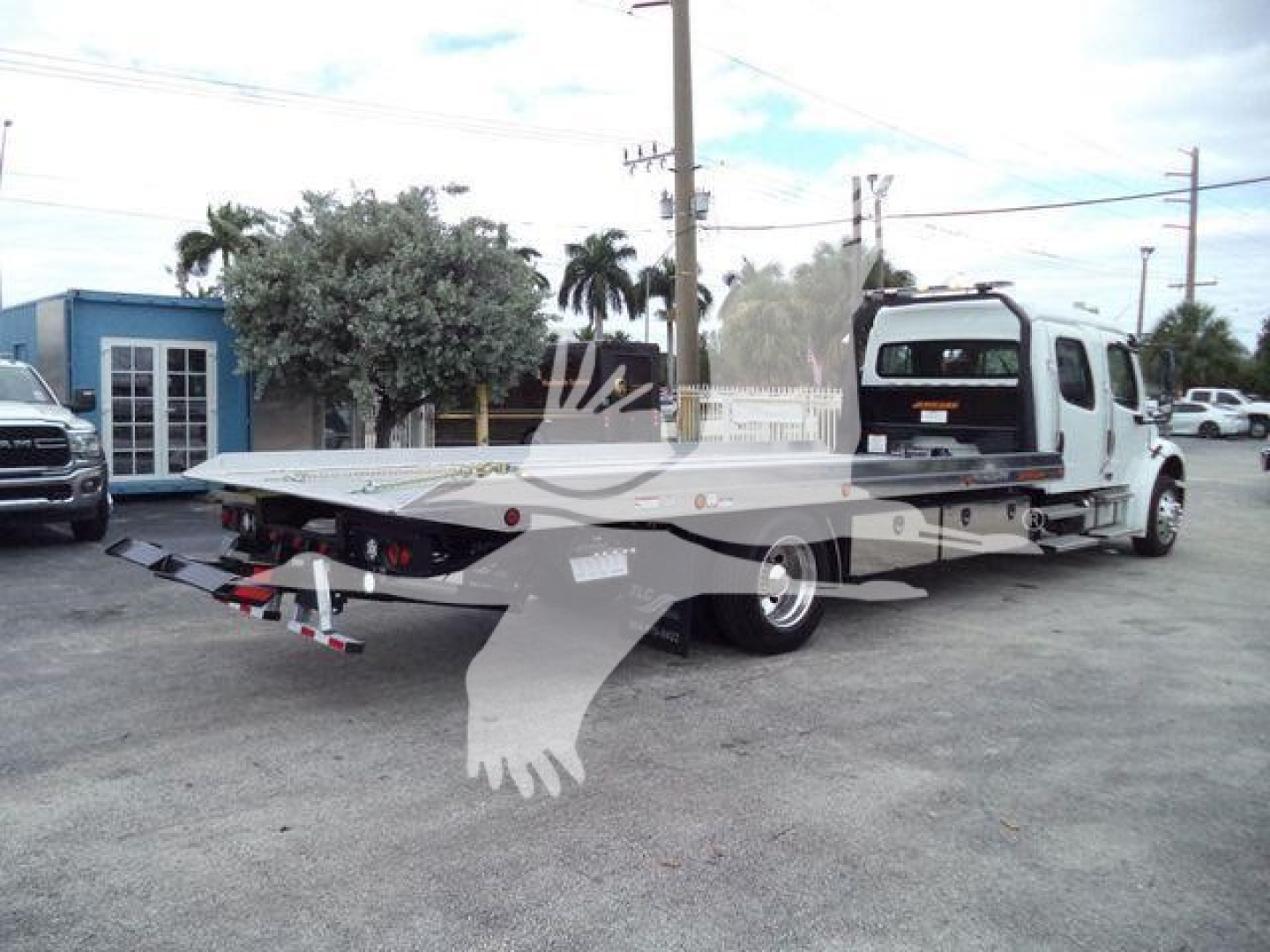Freightliner M2 106 rollback tow truck with flatbed, side view showing extended bed and rear towing apparatus.