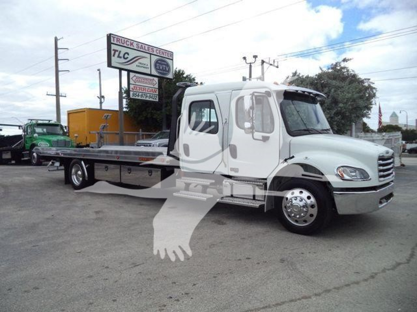 Truck: 2027 Freightliner M2 106 rollback truck showing white cab and flatbed, side view with dealership signage in background.