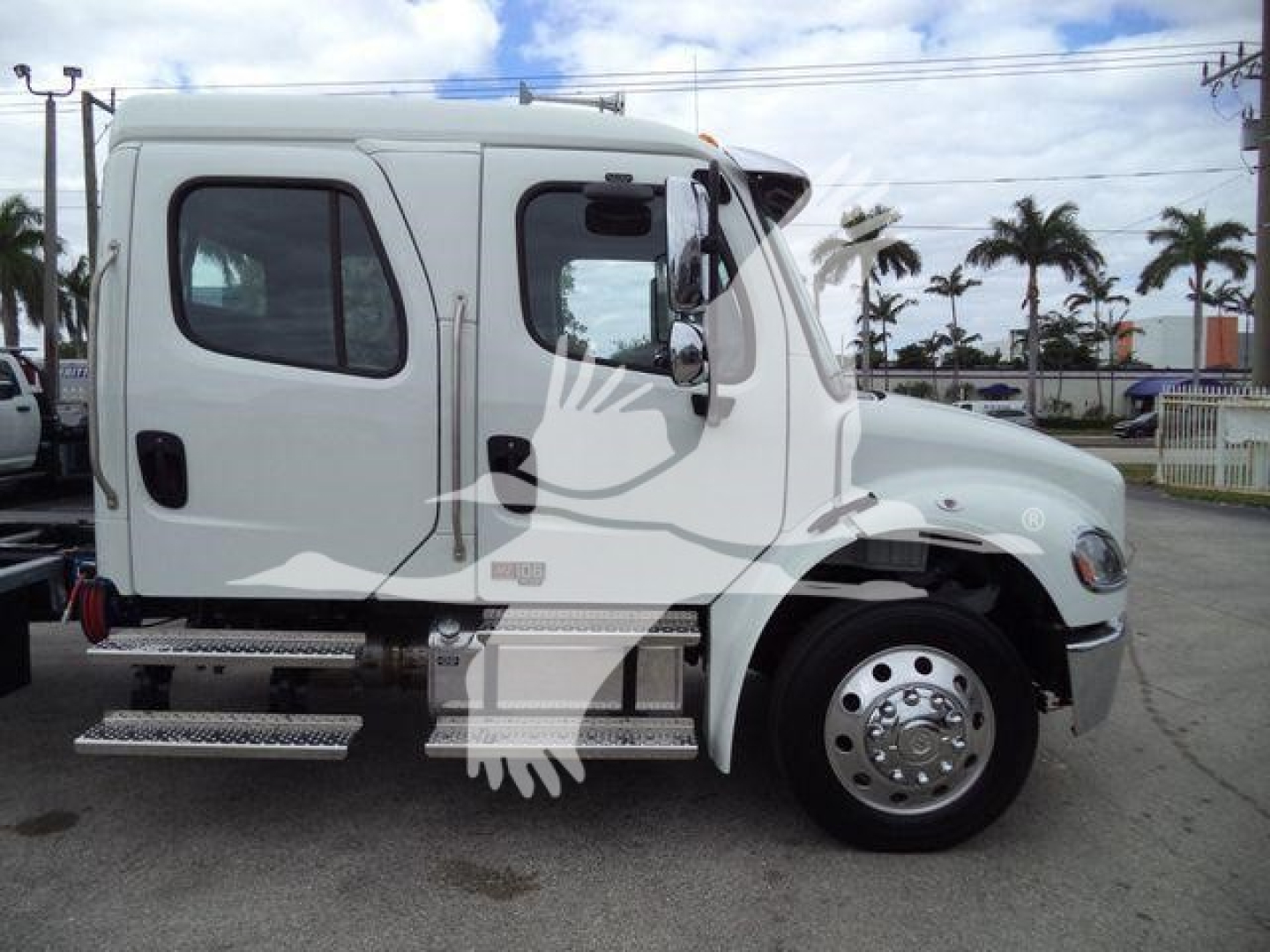Freightliner M2 106 rollback truck side view showing cab with door, large front wheel, chrome hubcap, and aluminum side steps.