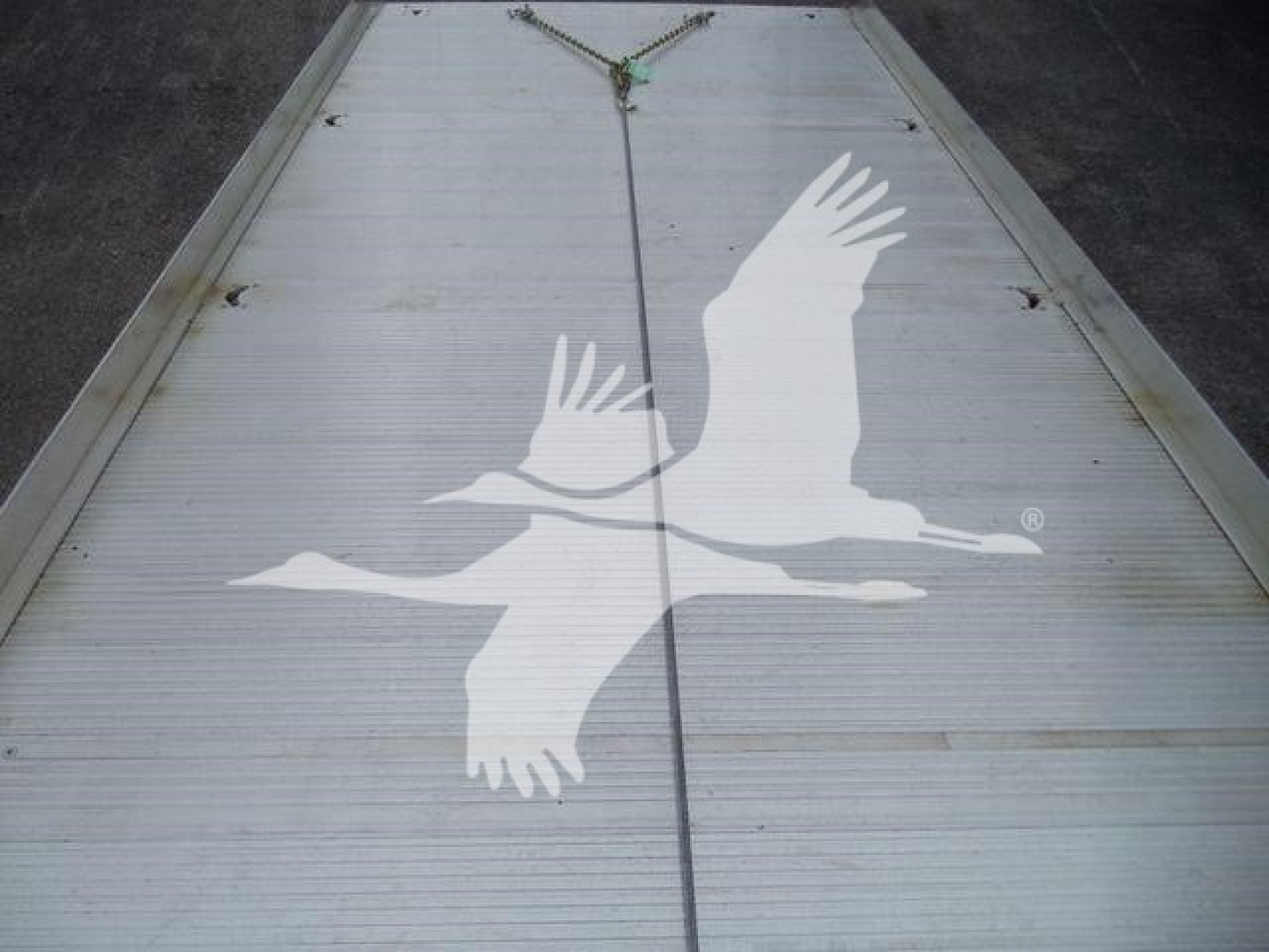 Flatbed trailer with Freightliner M2 106 branding featuring two white birds in flight graphic on the trailer door.