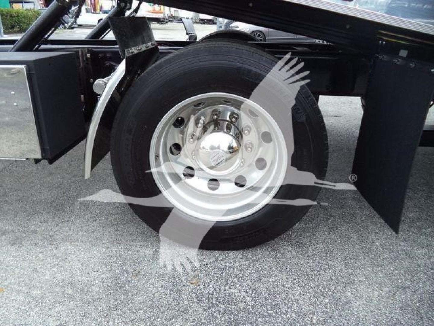 Freightliner M2 106 wheel and front suspension area showing steel alloy wheel and tire under trailer frame; mudflap and chassis components visible.